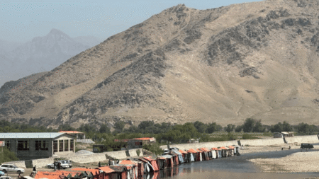 Photo of mountainous landscape in dry, hot conditions, with buildings and cars in the foreground along a river.