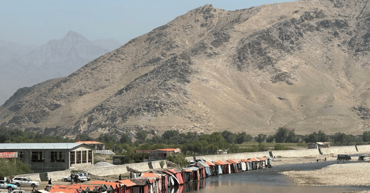 Photo of mountainous landscape in dry, hot conditions, with buildings and cars in the foreground along a river.