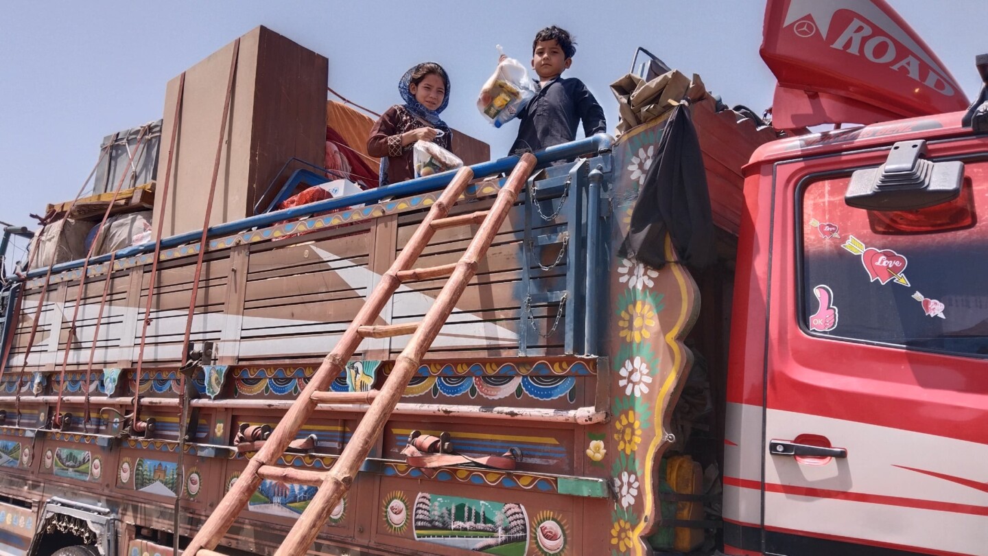 A colourful truck loaded with things. Two children are seen standing on top of the truck.