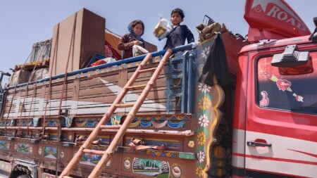 A colourful truck loaded with things. Two children are seen standing on top of the truck.