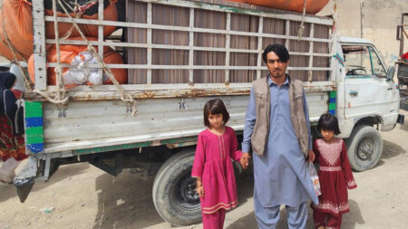 A man stands with his two young daughters in front of a fully loaded truck.
