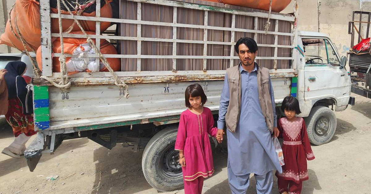 A man stands with his two young daughters in front of a fully loaded truck.