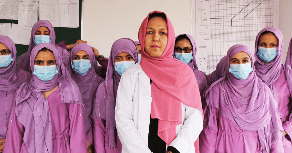 Hijabi women dressed in pink and purple clothes, wearing face masks and professional work clothes. At the front, in the middle, there is a woman in a white medical gown and pink hijab without a face mask.