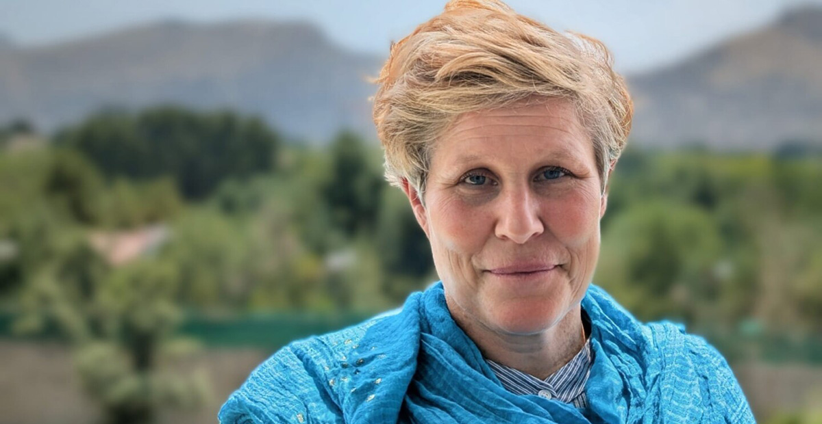 Porträttbild av kvinna med blå sjal om axlarna, stående med afghanska berg i bakgrunden.