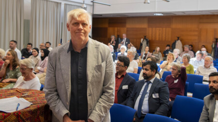 Man in front of a big meeting room full with people.