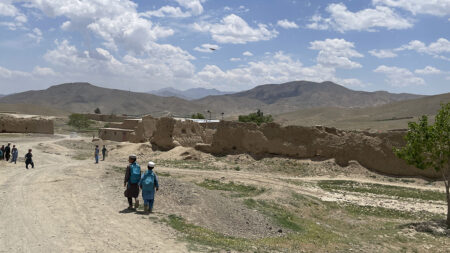 Schoolboys on a road in the Afghan countryside, with buildings close and mountains in the background.