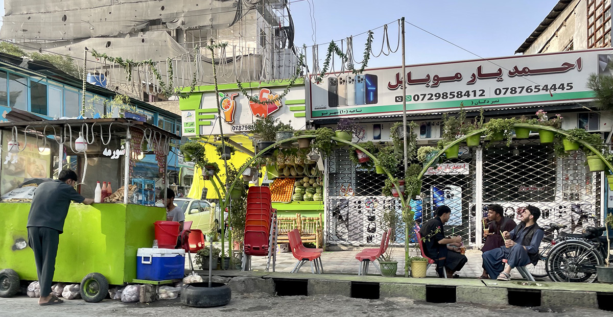 Street scene from Kabul with three young men talking to each other at a simple street cafe.