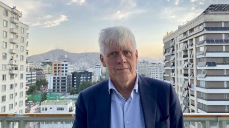 Man standing at a rooftop terrace in front of Kabul city and the mountains in the background.