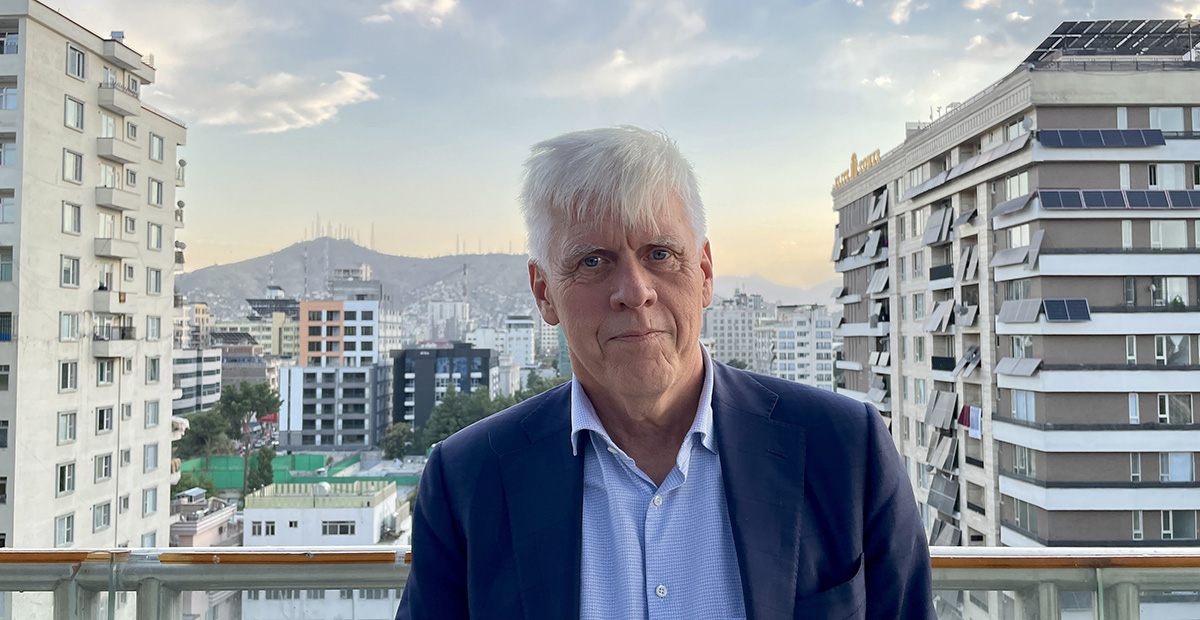 Man standing at a rooftop terrace in front of Kabul city and the mountains in the background.