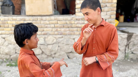 Two boys in orange clothes are communicating with each other in sign language outside a house.