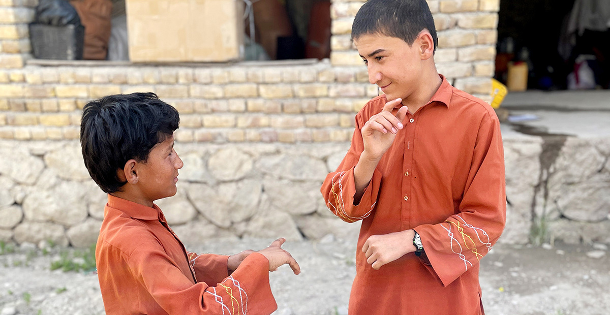 Two boys in orange clothes are communicating with each other in sign language outside a house.